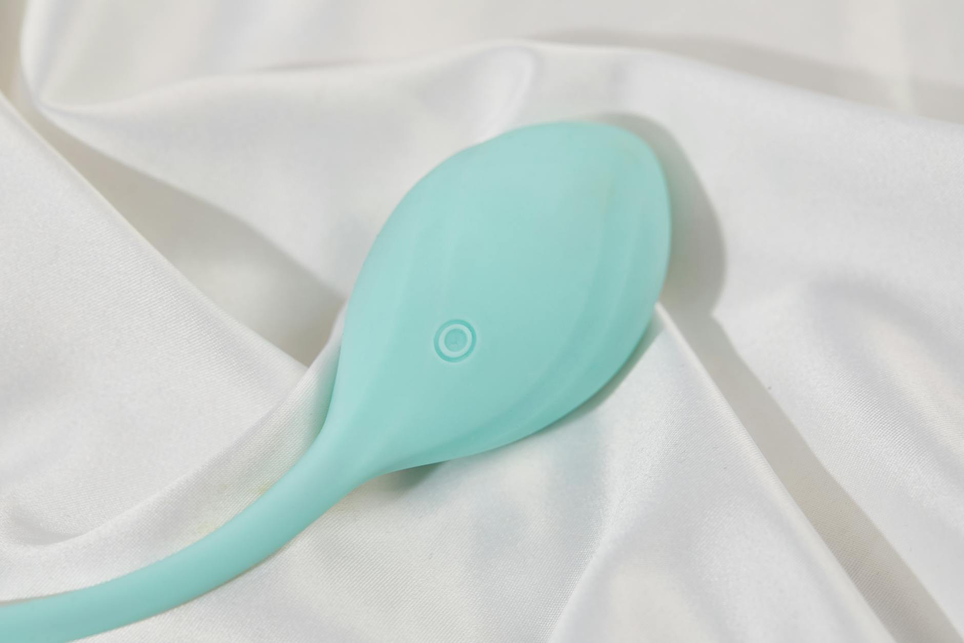 A teal lemon vibrator resting on white silk, showing smooth ergonomic design