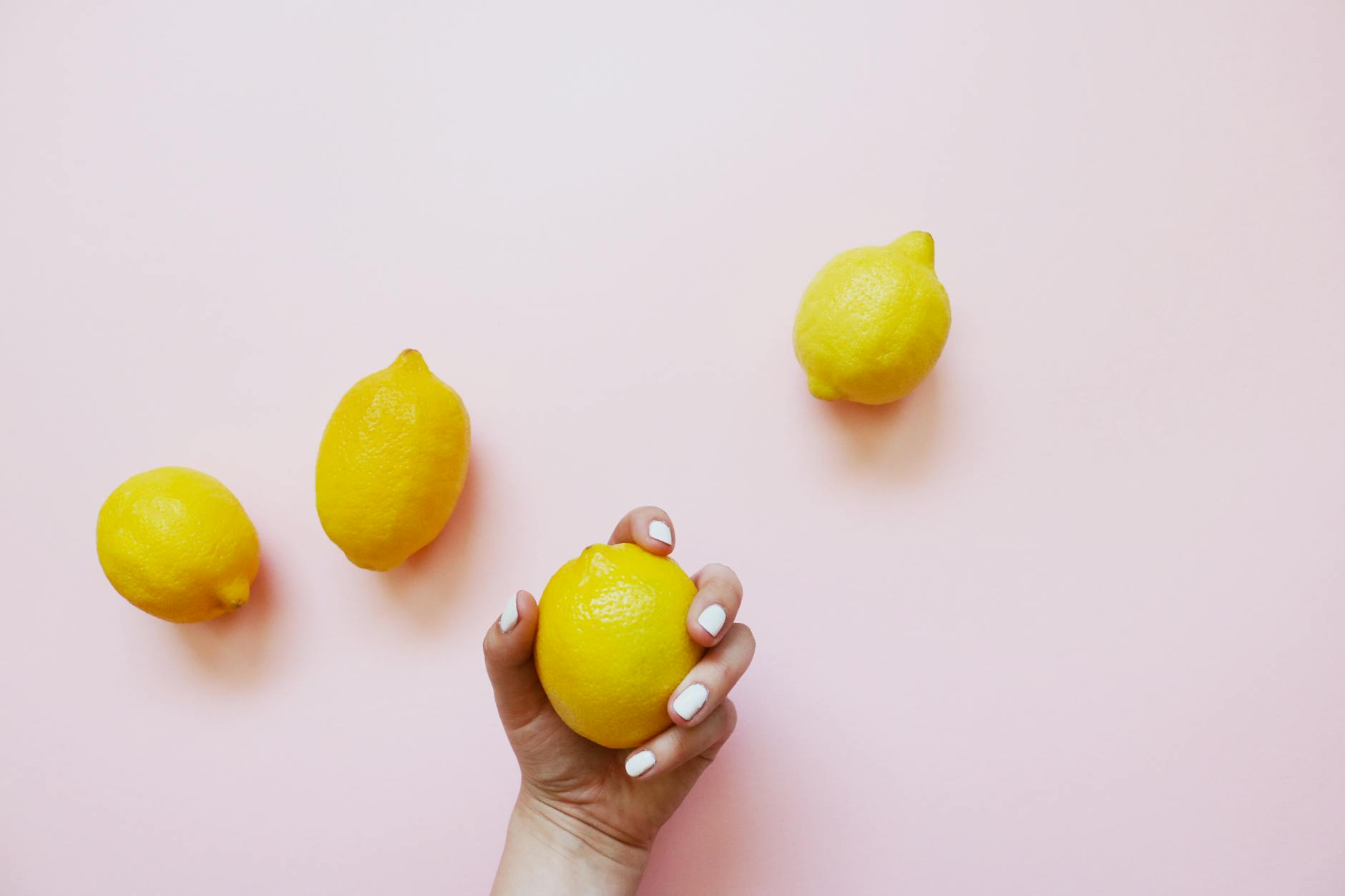A hand holding a bright lemon on a soft pink background, symbolizing the gentle sensation of air-suction pleasure.