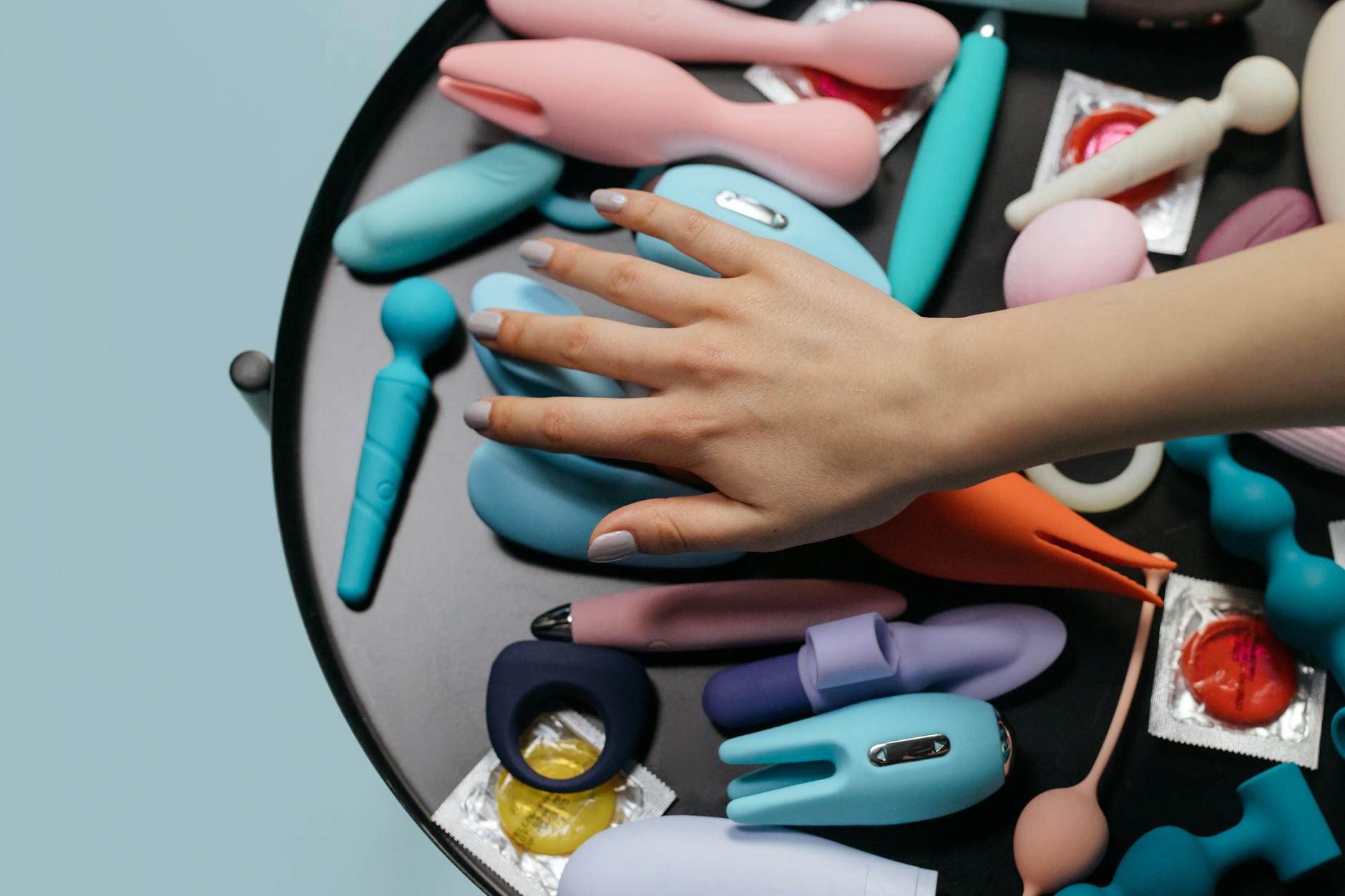 Two hands holding silicone vibrators against a pastel background