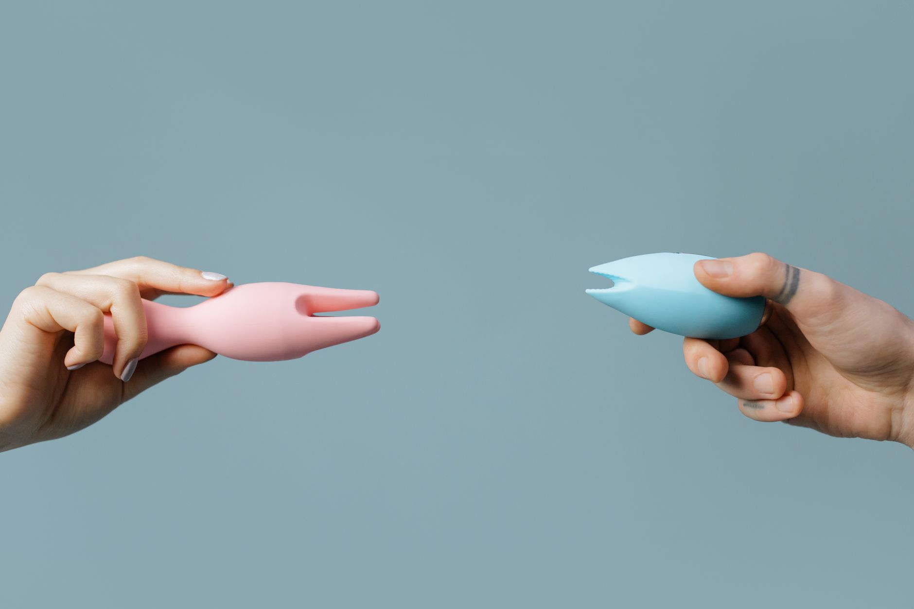 Two hands holding pink and blue clitoral vibrators against a pastel background, representing renewed pleasure and self-care.
