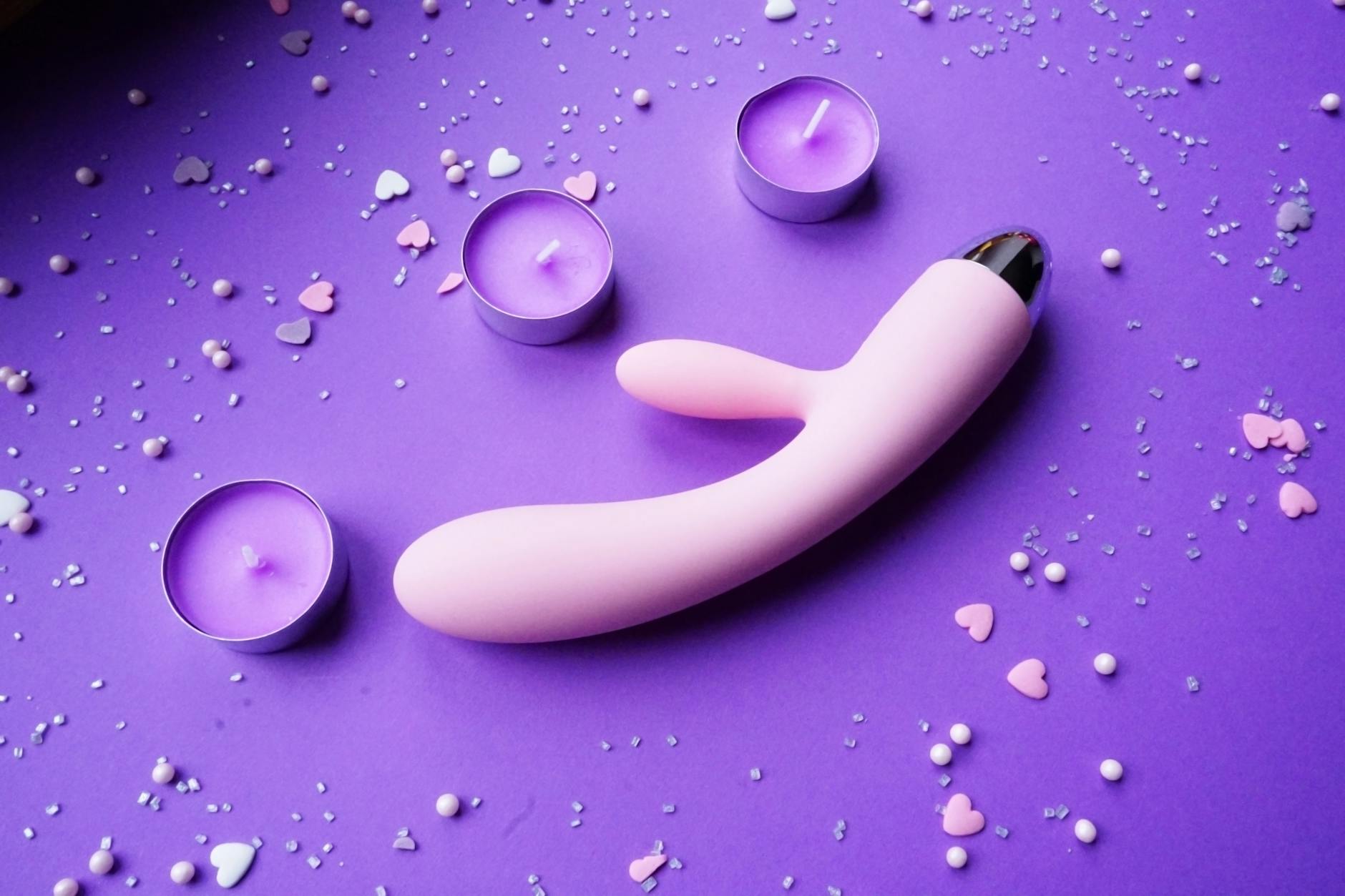 Pink vibrator on purple background with heart confetti and candles for intimate moments